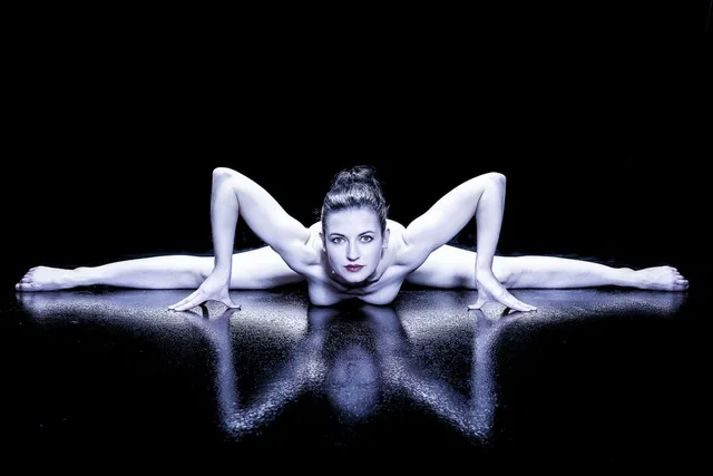 Symmetrische Pose auf spiegelndem Boden mit hellem Gesicht und dunklem Hintergrund.