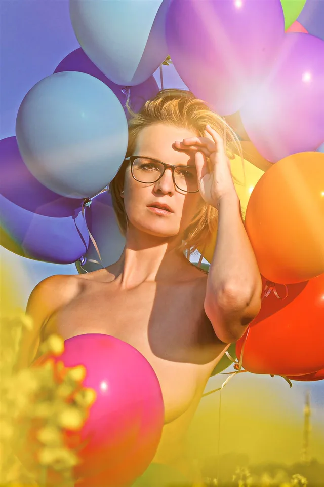 Portrait einer Frau mit Brille zwischen bunten Luftballons.