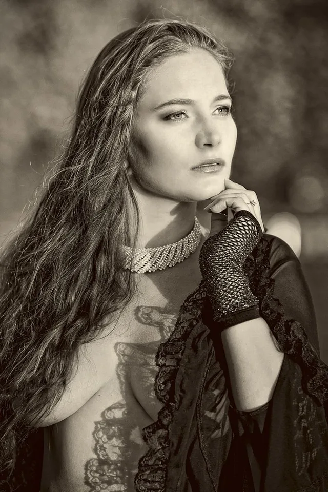 Sepiafarbenes Portrait einer Frau mit langem Haar und schwarzer Spitze, den Kopf auf die Hand gestützt.