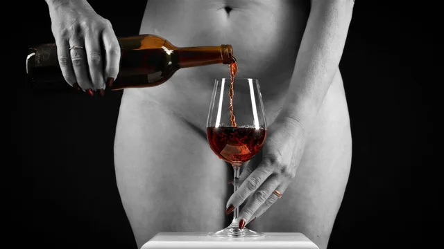 Schwarzweißaufnahme eines Körpers mit Flasche und rot gefärbtem Wein im Glas.