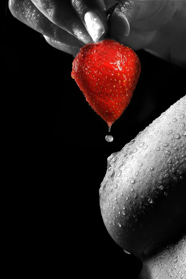 Schwarzweißes Körperdetail mit einer rot gefärbten Erdbeere und einem Wassertropfen.